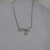 A silver chain necklace with a bow-shaped pendant and a single freshwater pearl.
