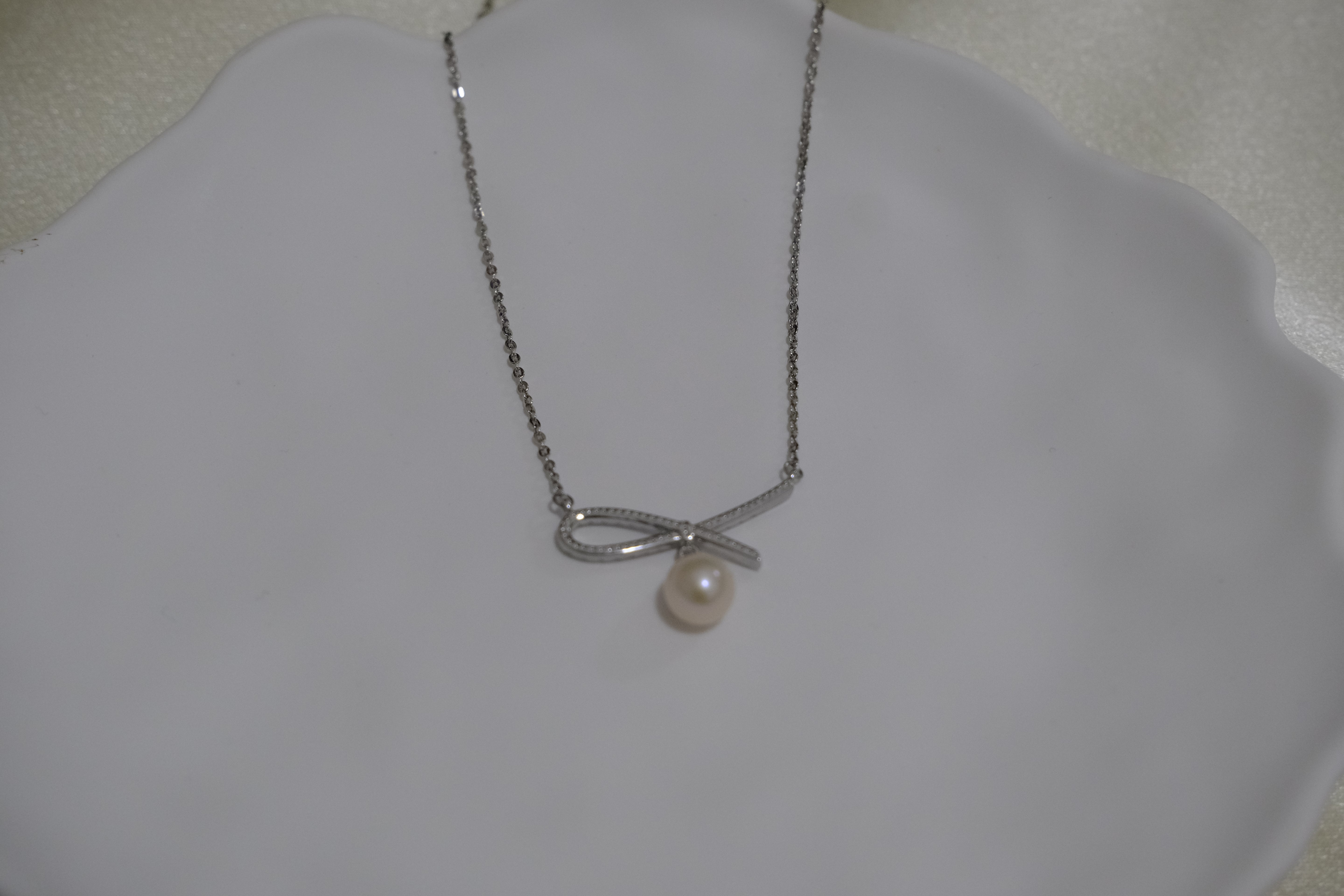 A silver chain necklace with a bow-shaped pendant and a single freshwater pearl.