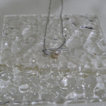 A silver bow pendant necklace with a single freshwater pearl on a textured white surface.