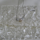 A silver bow pendant necklace with a single freshwater pearl on a textured white surface.