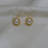 Round freshwater pearl earrings with gold-plated circular frames on a white fabric.