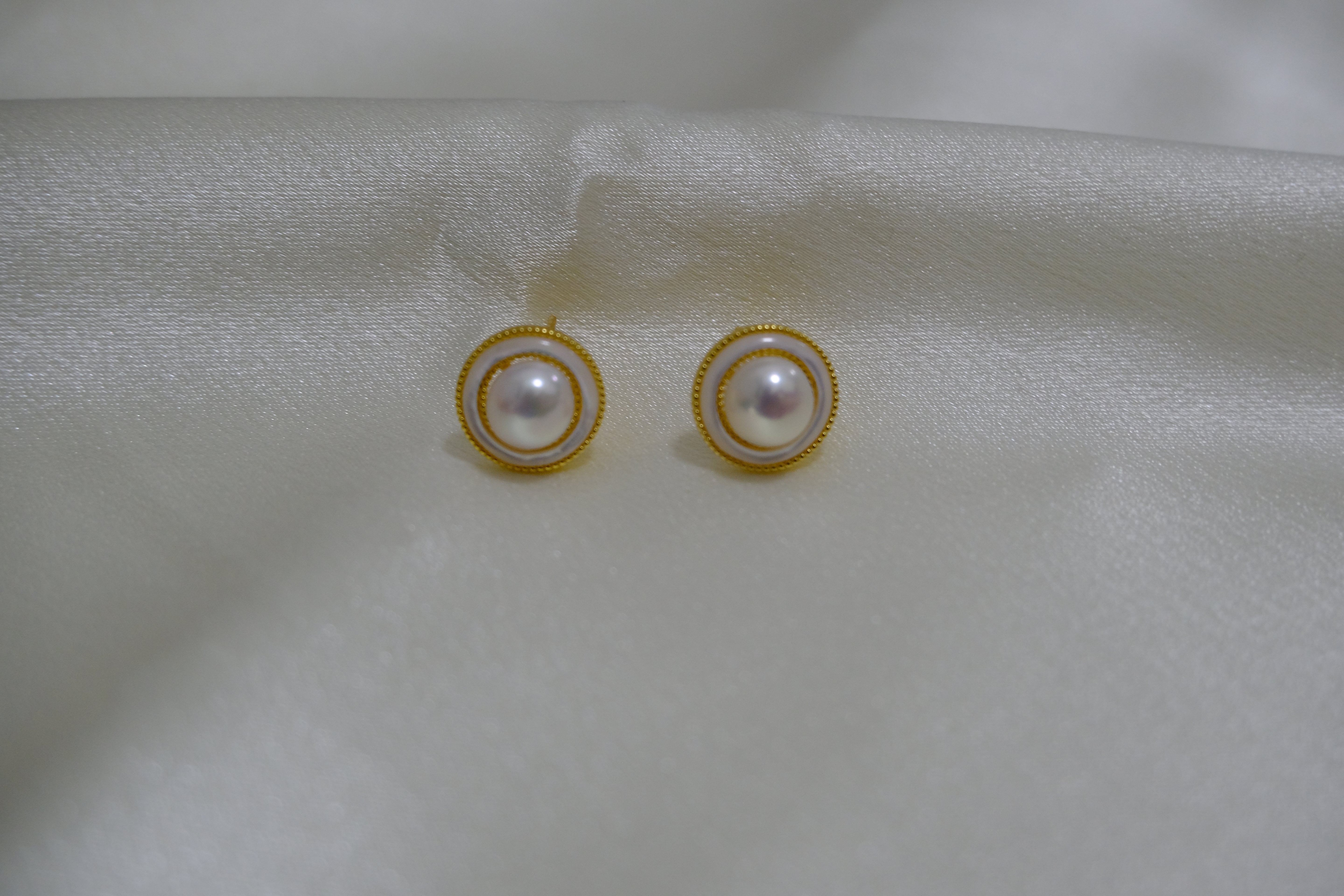 Round freshwater pearl earrings with gold-plated circular frames on a white fabric.