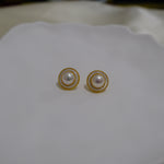 Round freshwater pearl earrings with a gold-plated circular frame on a white surface.