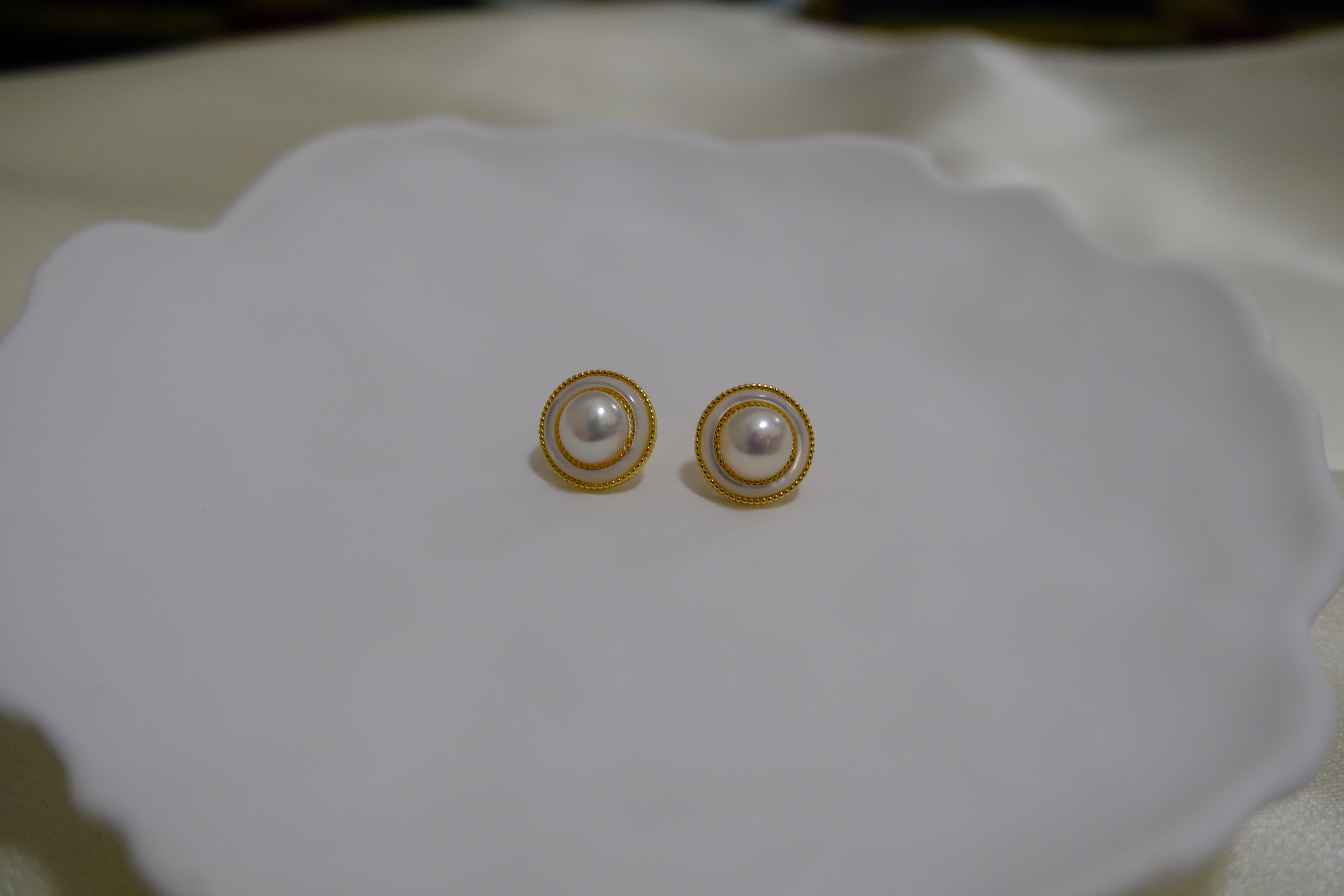 Round freshwater pearl earrings with a gold-plated circular frame on a white surface.