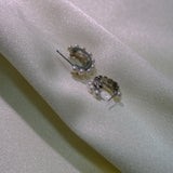 Two silver half-hoop earrings with small pearls are displayed on a light fabric.