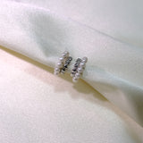 Two silver half-hoop earrings with small pearls are displayed on a white fabric.