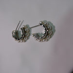 Two silver half-hoop earrings with small white pearls are displayed on a white surface.