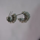 Two silver half-hoop earrings with small white pearls are displayed on a white surface.
