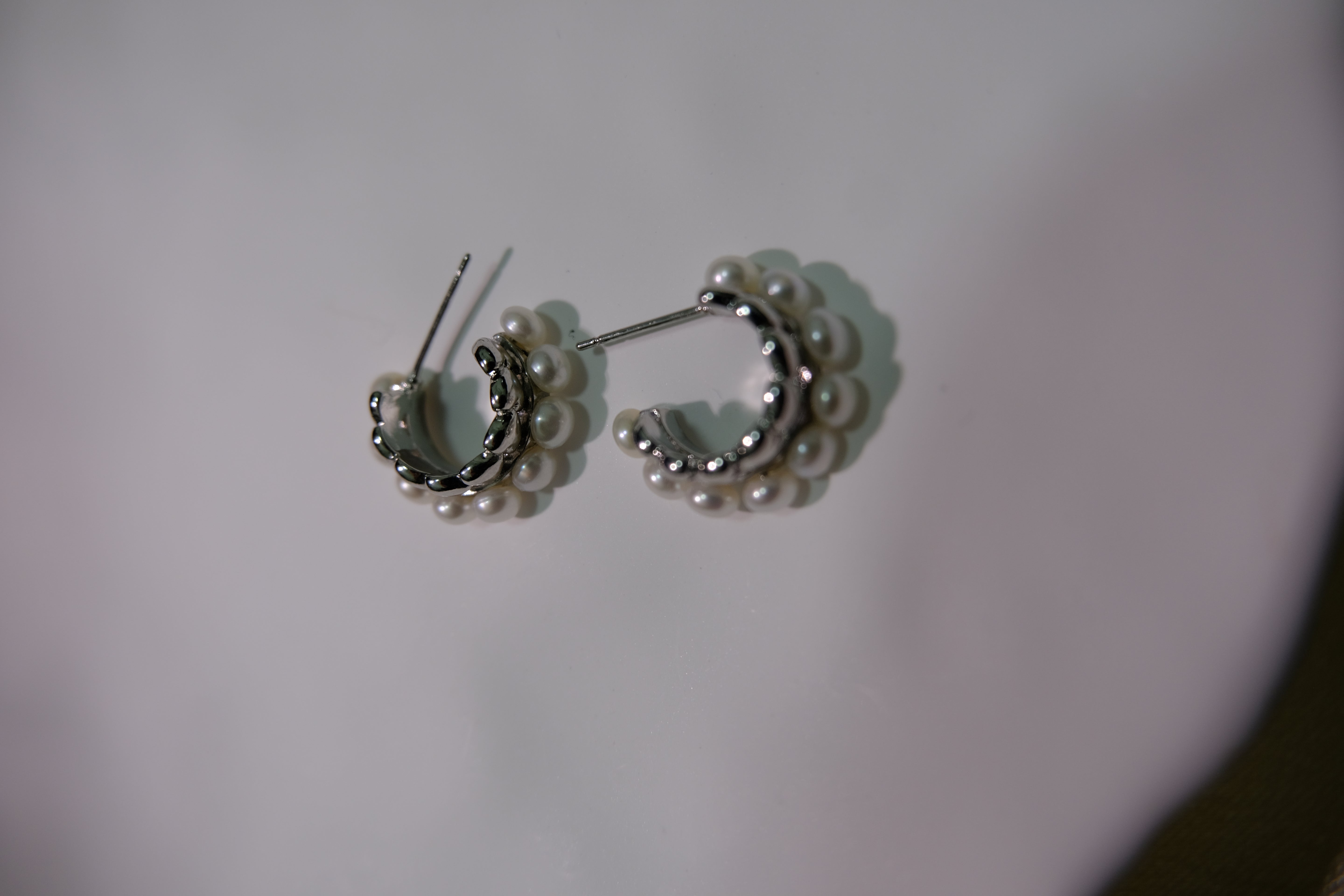 Two silver half-hoop earrings with small white pearls are displayed on a white surface.