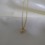 A gold chain necklace with three small, irregularly shaped pearls in white and peach.