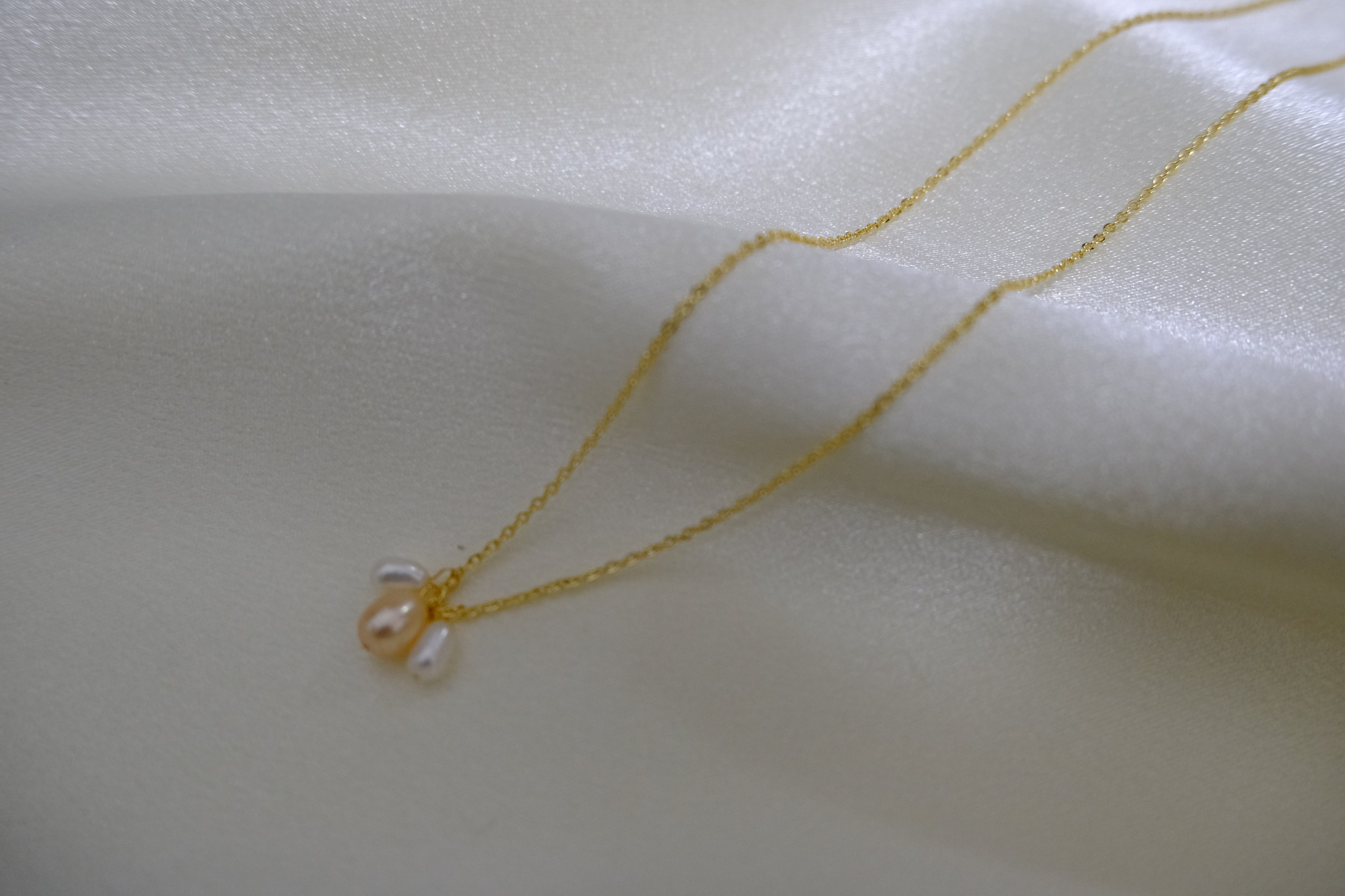 Gold chain necklace with three small, irregularly shaped pearls.