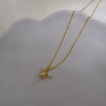 A gold chain necklace with three freshwater pearls, one peach and two white.