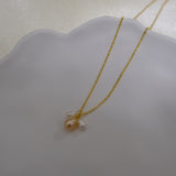 A gold chain necklace with three freshwater pearls, one peach and two white.