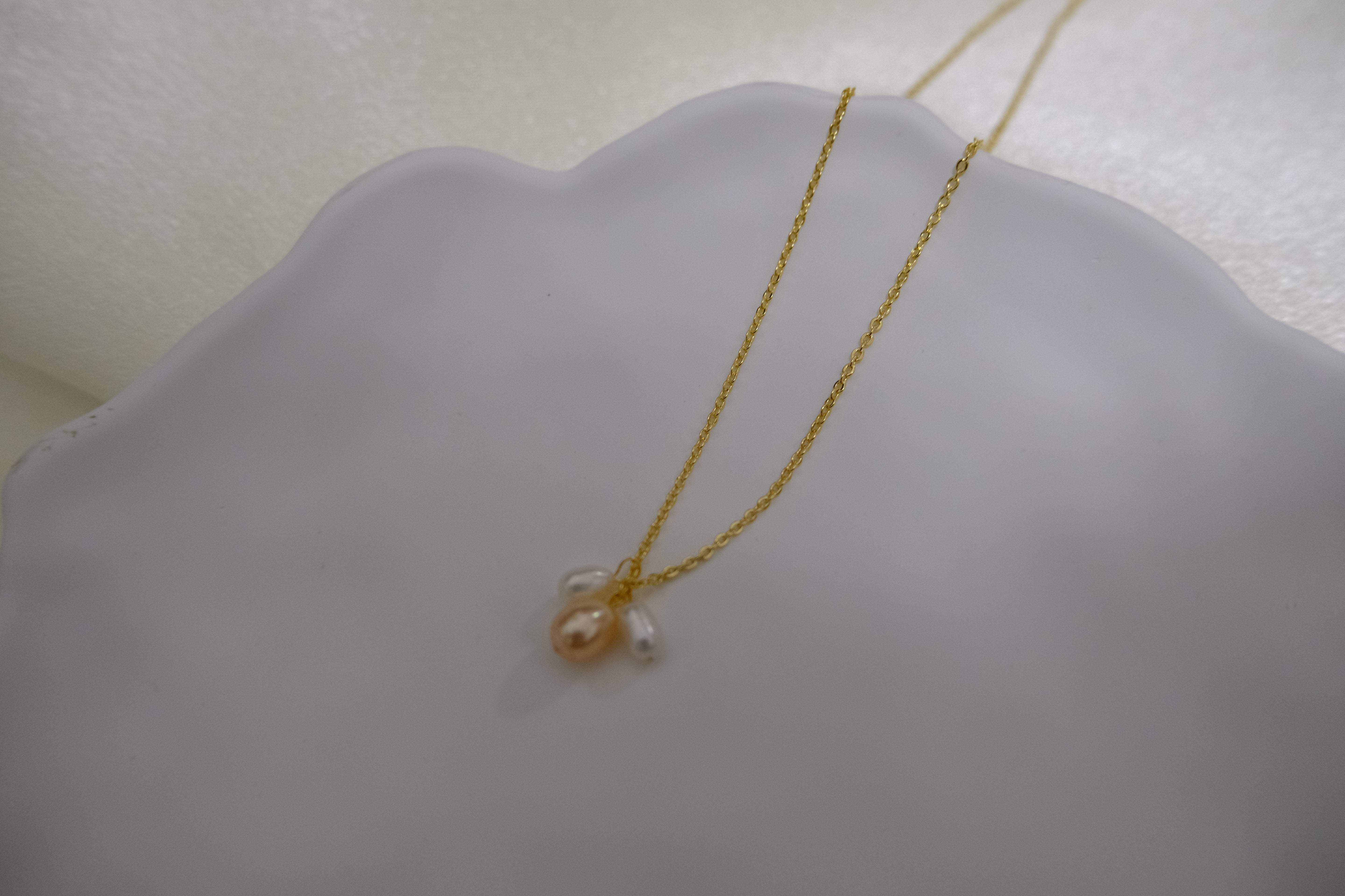 A gold chain necklace with three freshwater pearls, one peach and two white.