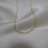 A delicate gold chain necklace with seven small, oval white pearls in the center.