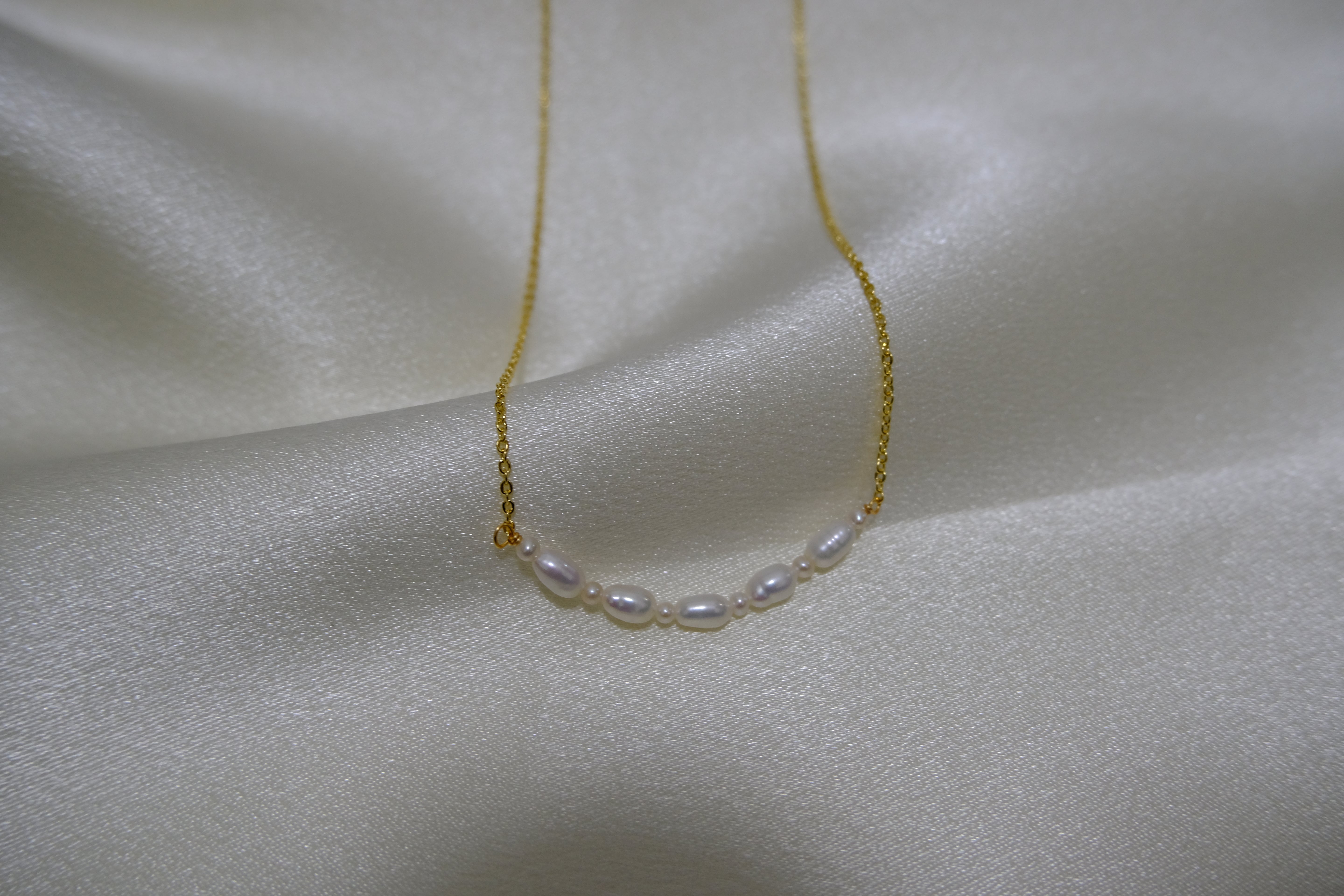 A delicate gold chain necklace with seven small, oval white pearls in the center.