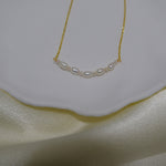 A delicate gold chain necklace with a row of small, oval freshwater pearls.