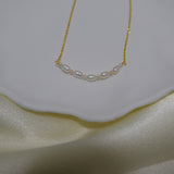 A delicate gold chain necklace with a row of small, oval freshwater pearls.