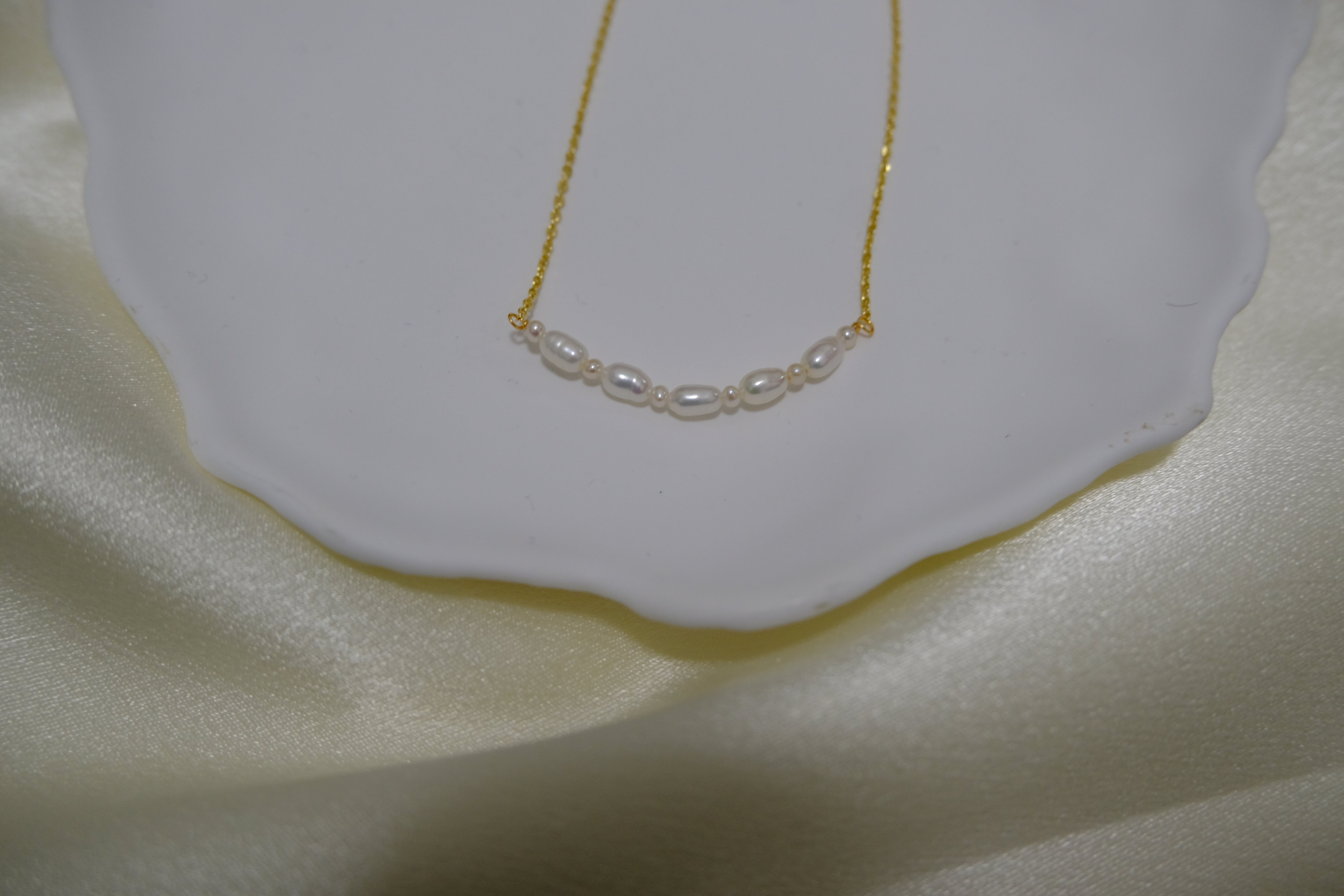 A delicate gold chain necklace with a row of small, oval freshwater pearls.