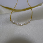 A delicate gold chain necklace with seven small white pearls is displayed on a white cloth.