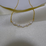 A delicate gold chain necklace with seven small white pearls is displayed on a white cloth.