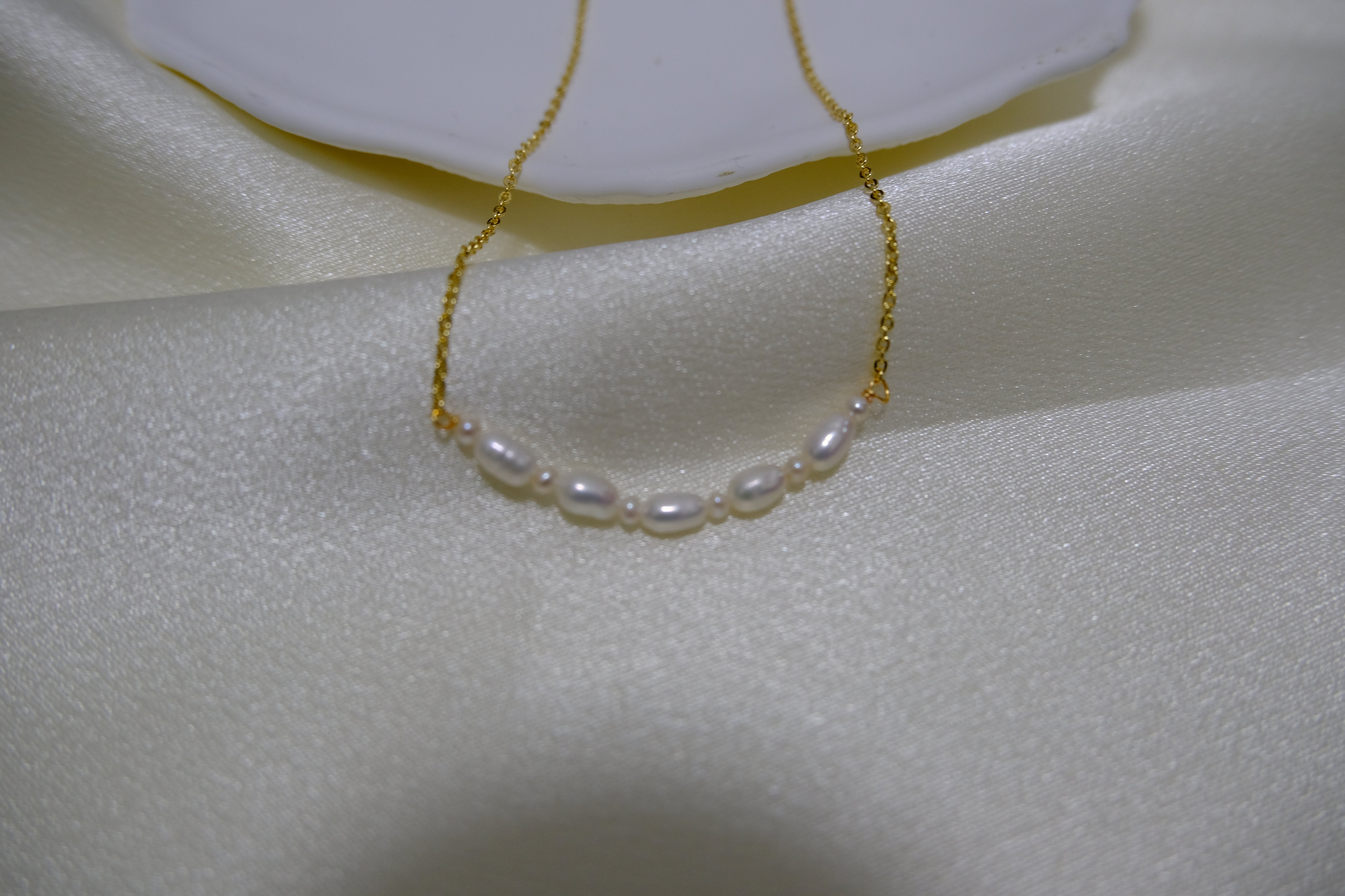 A delicate gold chain necklace with seven small white pearls is displayed on a white cloth.