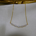 A delicate gold chain necklace features a curved line of small white pearls.