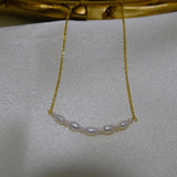A delicate gold chain necklace features a curved line of small white pearls.