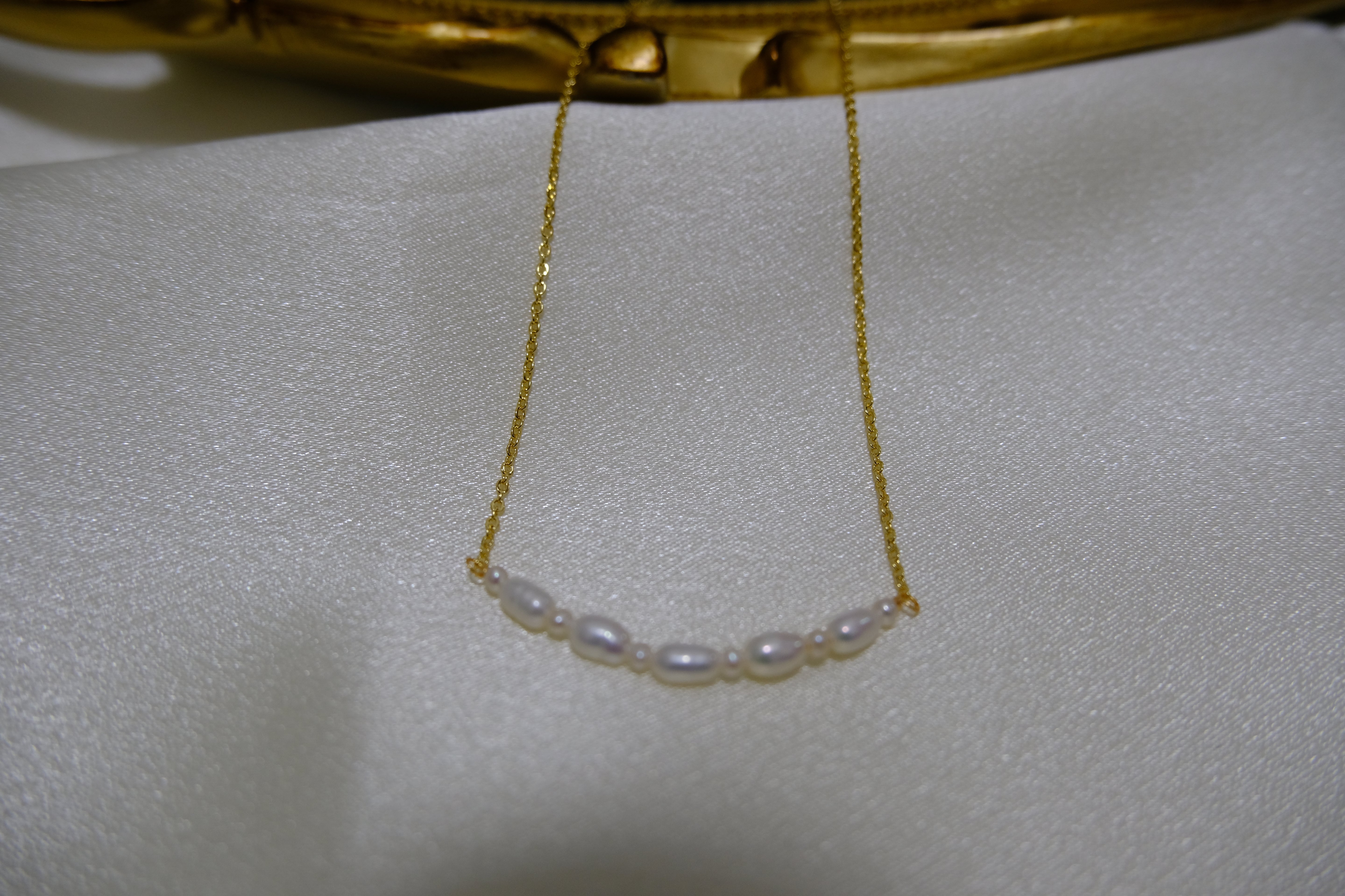 A delicate gold chain necklace features a curved line of small white pearls.