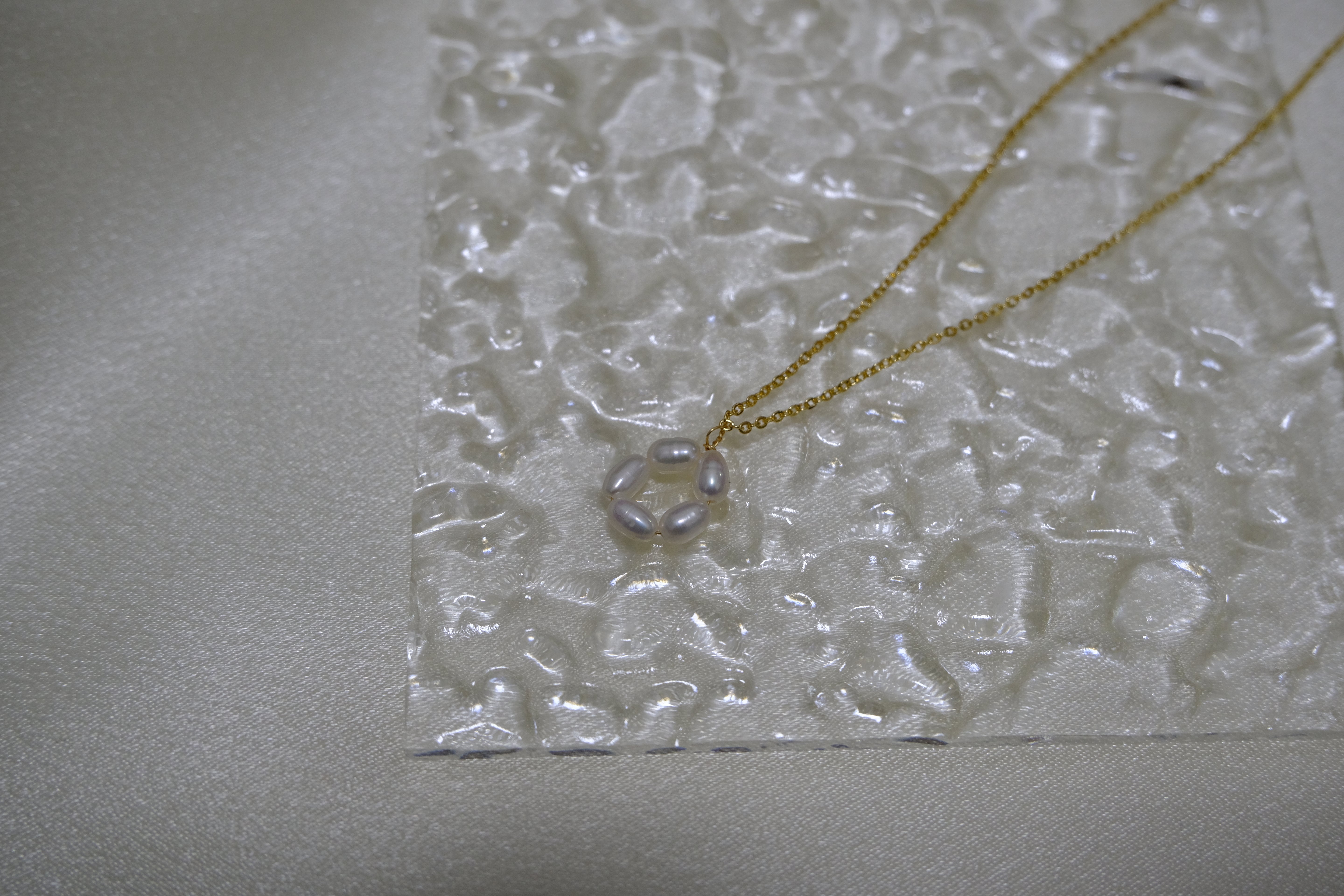 A gold-plated necklace features a pendant of five freshwater pearls arranged in a flower shape.