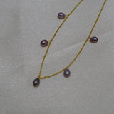 Dainty gold-plated necklace featuring five purple freshwater pearls on a light background.