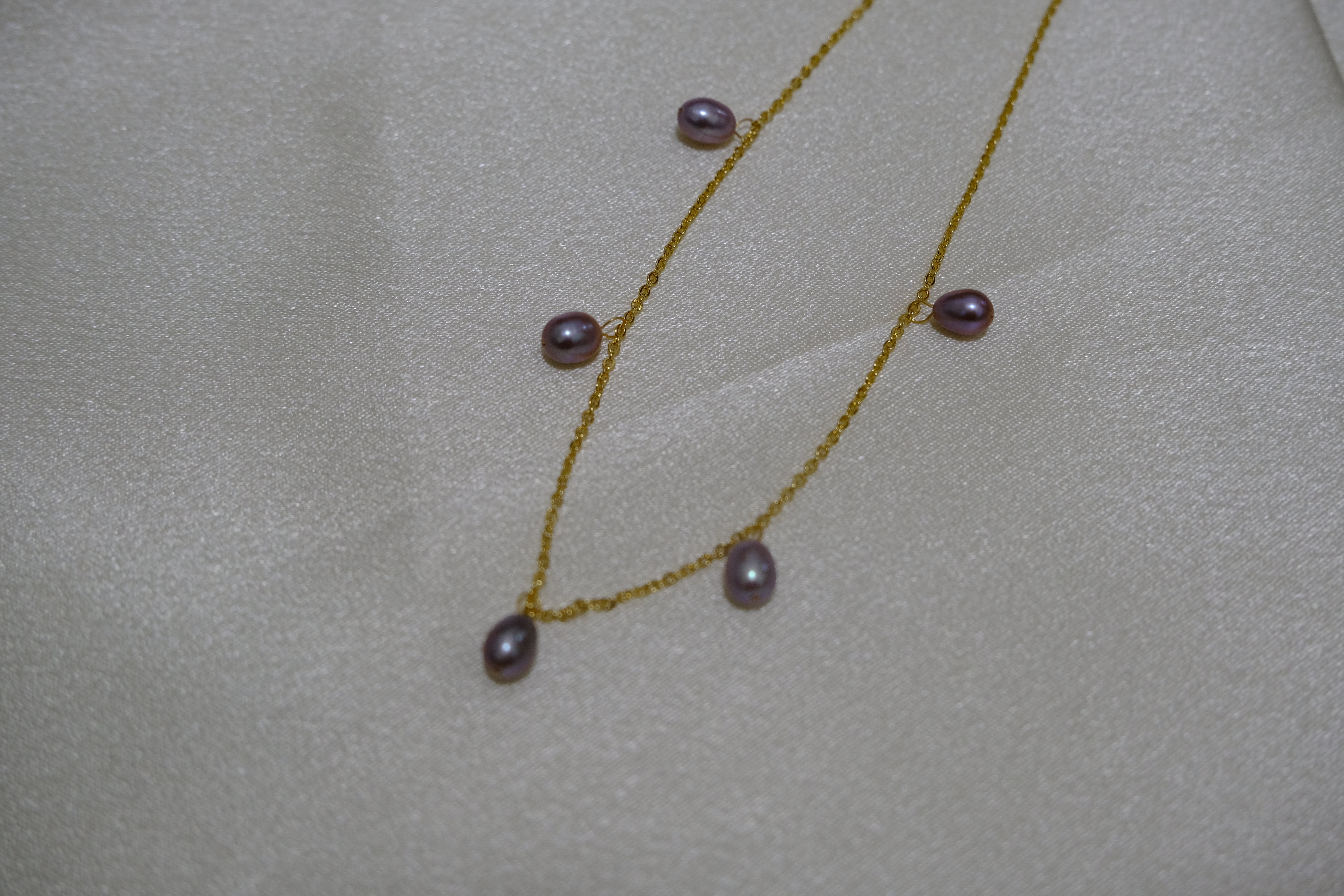 Dainty gold-plated necklace featuring five purple freshwater pearls on a light background.