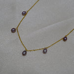 Dainty gold-plated necklace with seven small, lustrous purple pearls on a light background.