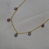 Dainty gold-plated necklace with seven small, lustrous purple pearls on a light background.