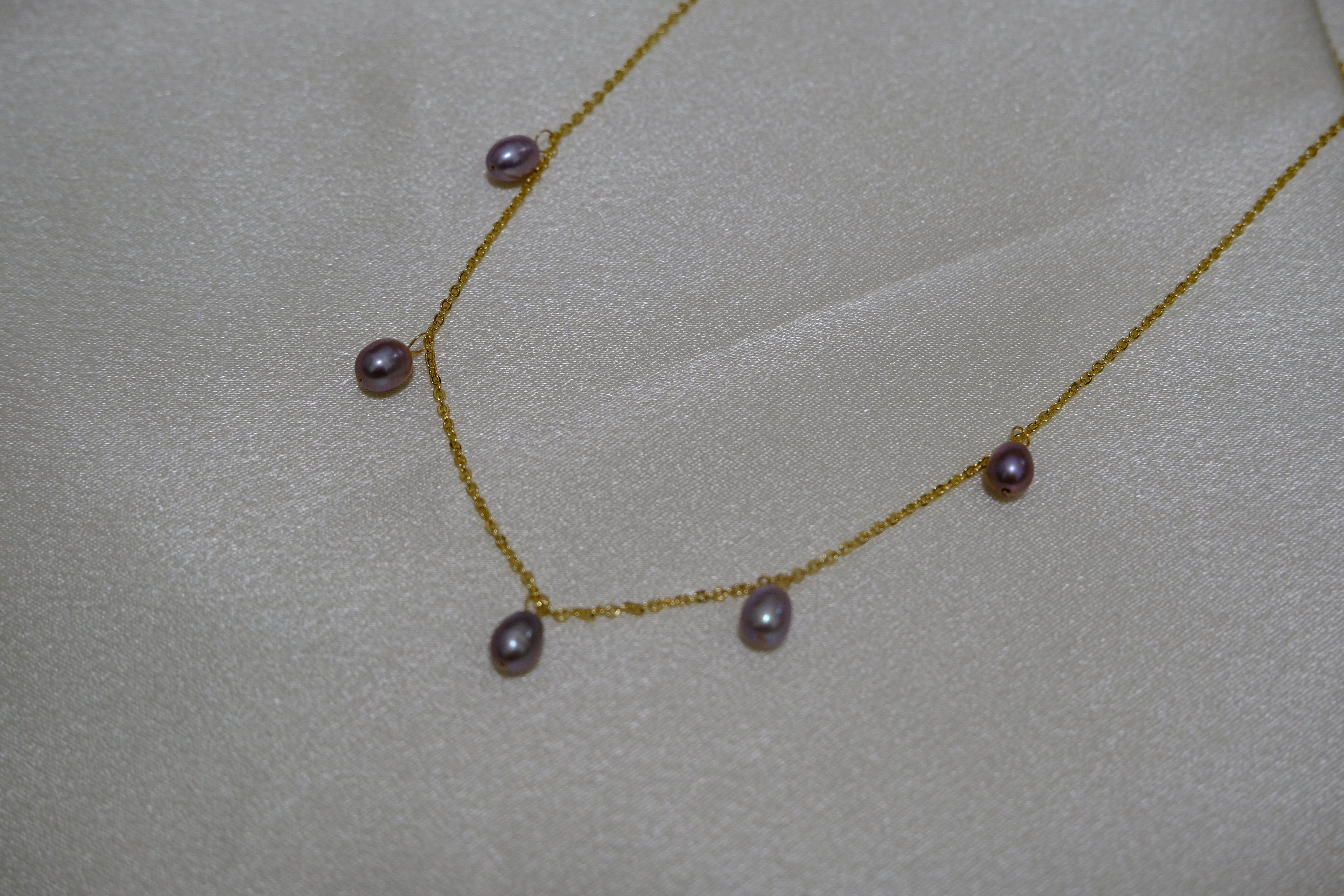 Dainty gold-plated necklace with seven small, lustrous purple pearls on a light background.