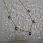 Dainty gold-plated necklace with five purple freshwater pearls on a textured white surface.