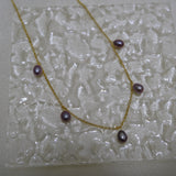 Dainty gold-plated necklace with five purple freshwater pearls on a textured white surface.
