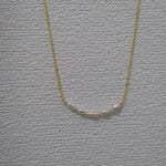 A gold chain necklace with a row of small, white freshwater pearls.