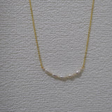 A gold chain necklace with a row of small, white freshwater pearls.