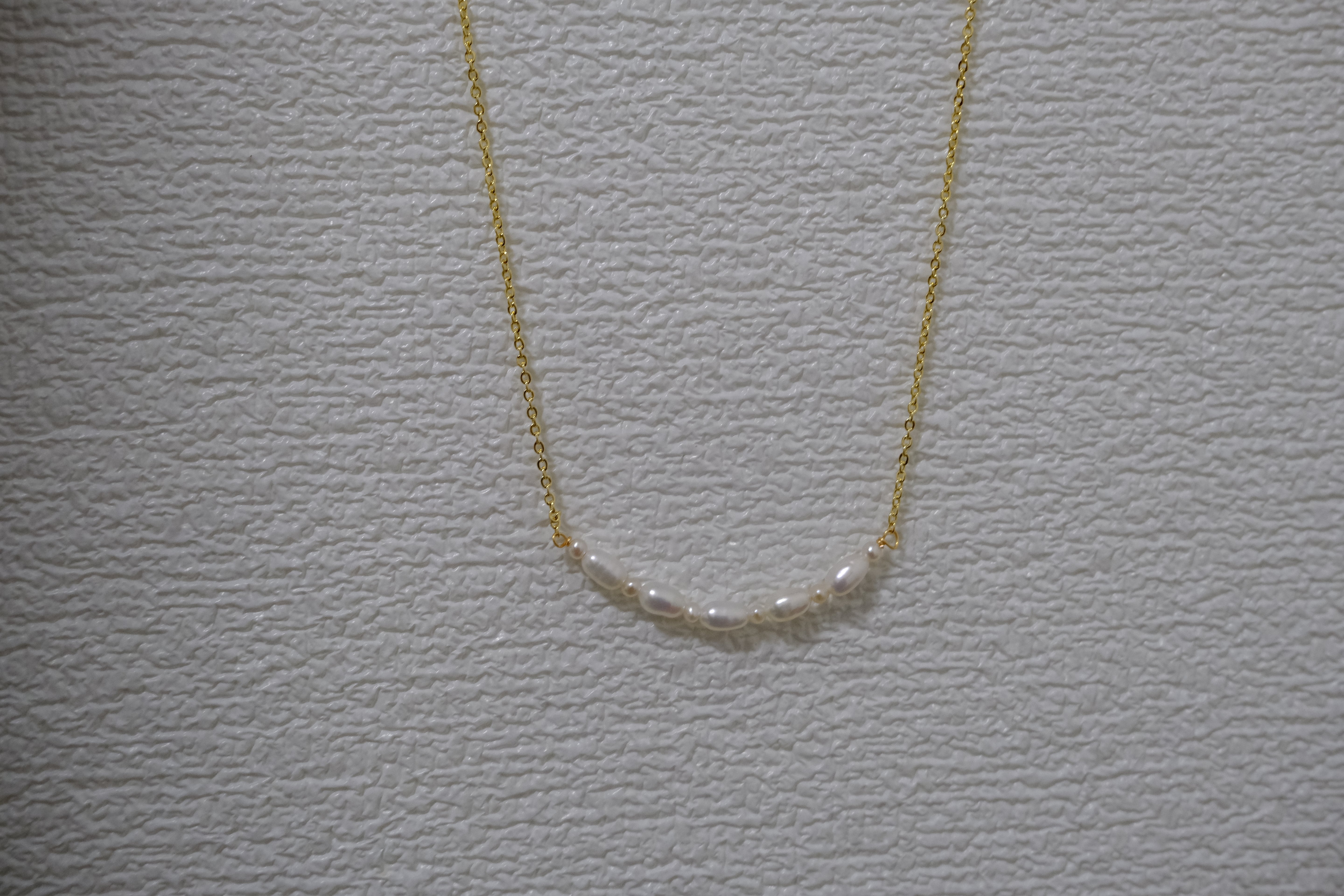 A gold chain necklace with a row of small, white freshwater pearls.