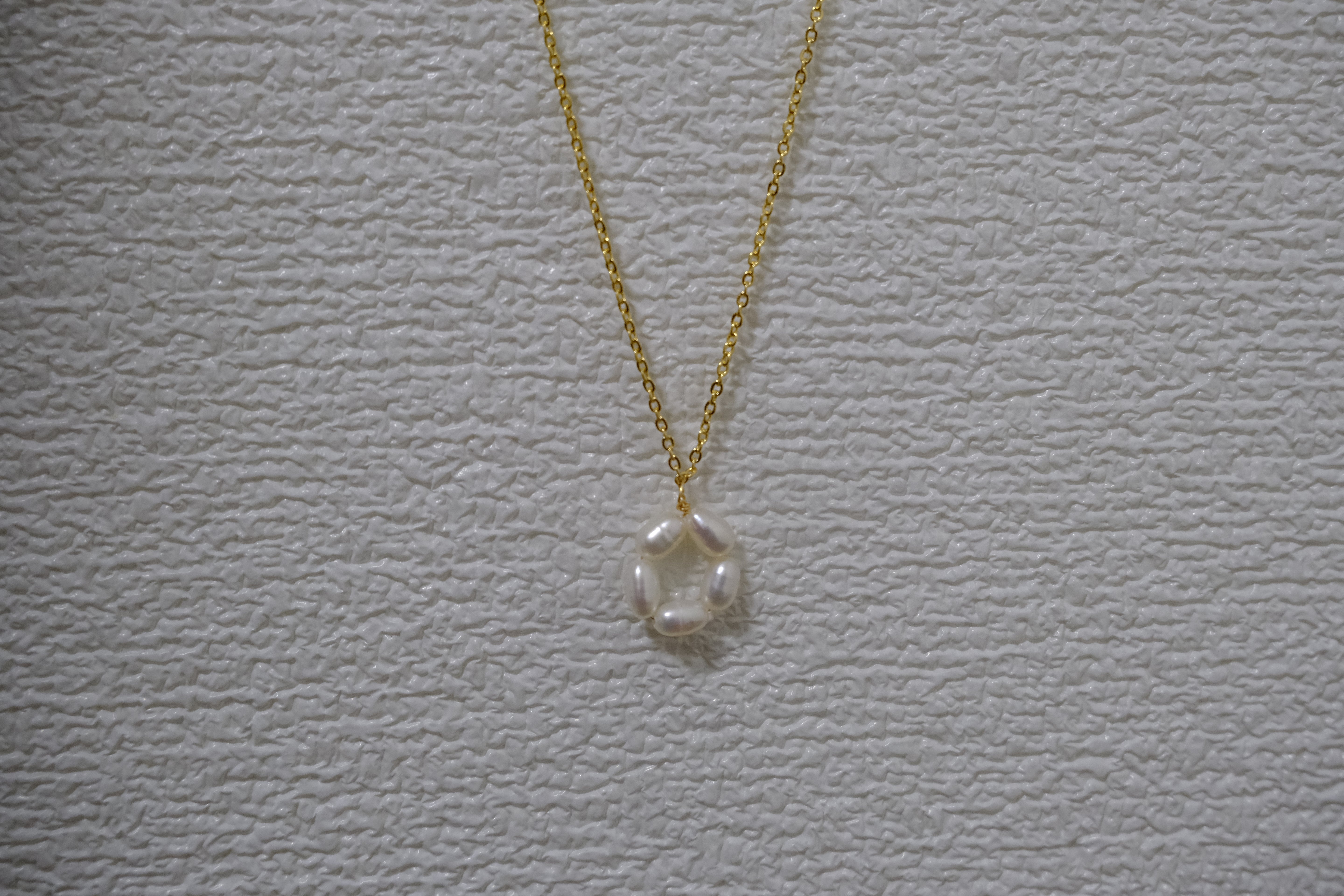A gold-plated necklace features a pendant of five freshwater pearls arranged in a flower shape.