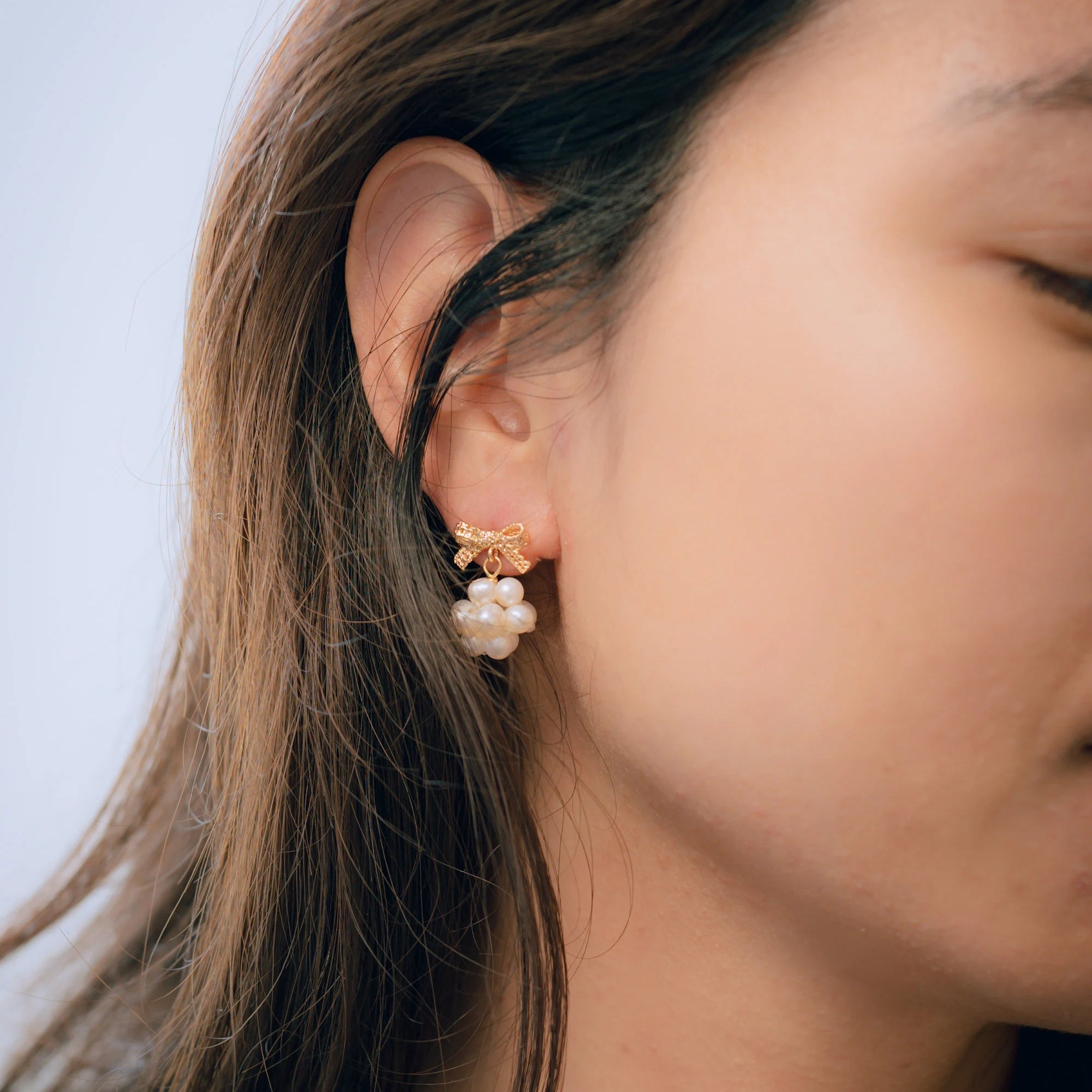 Gold-plated bowknot dangle freshwater pearl earring on a woman's ear.