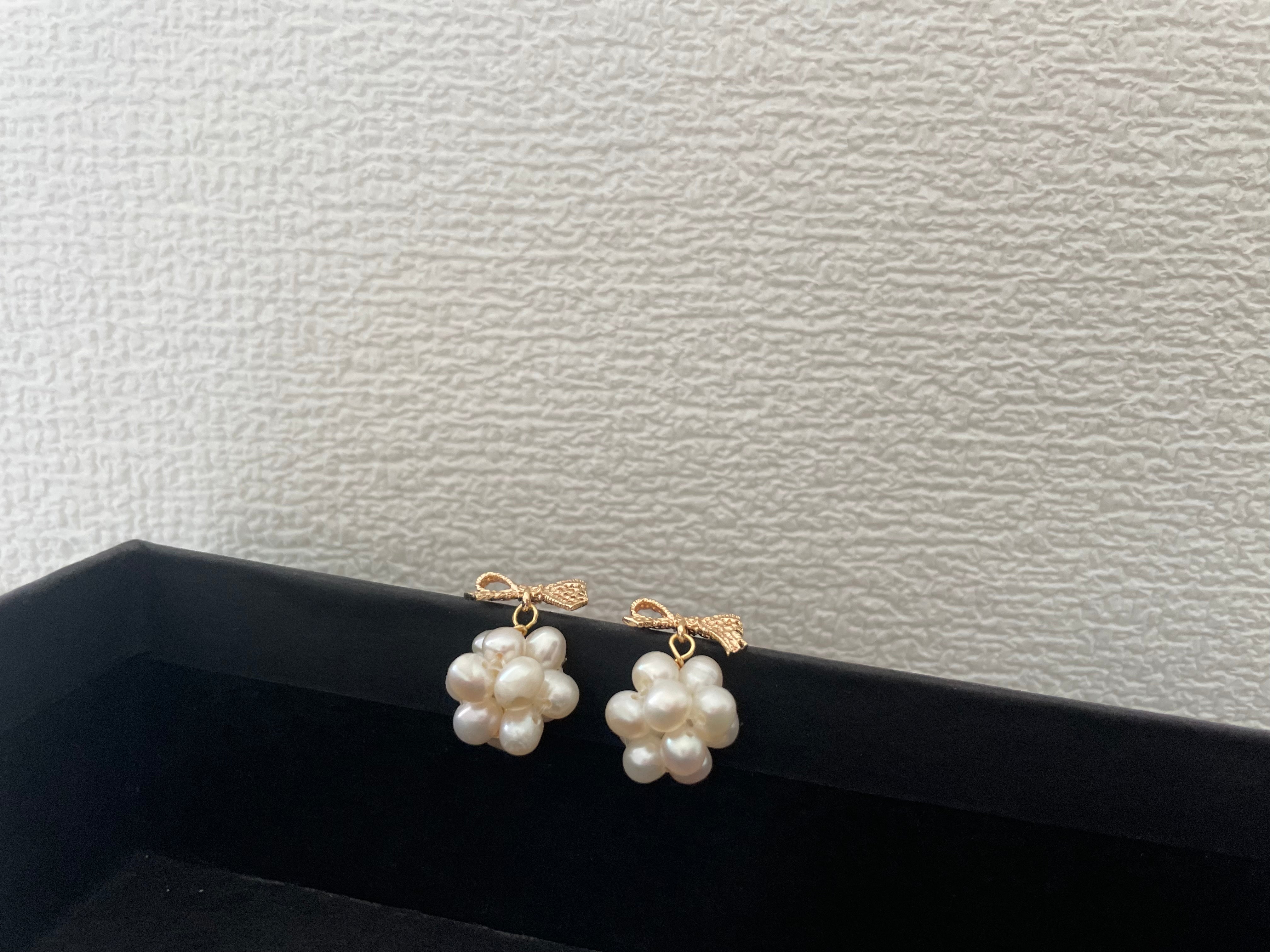 Gold-plated bowknot dangle freshwater pearl earrings are displayed on a black surface.