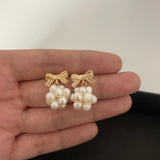 Gold-plated bowknot dangle earrings with clusters of freshwater pearls held in a hand.