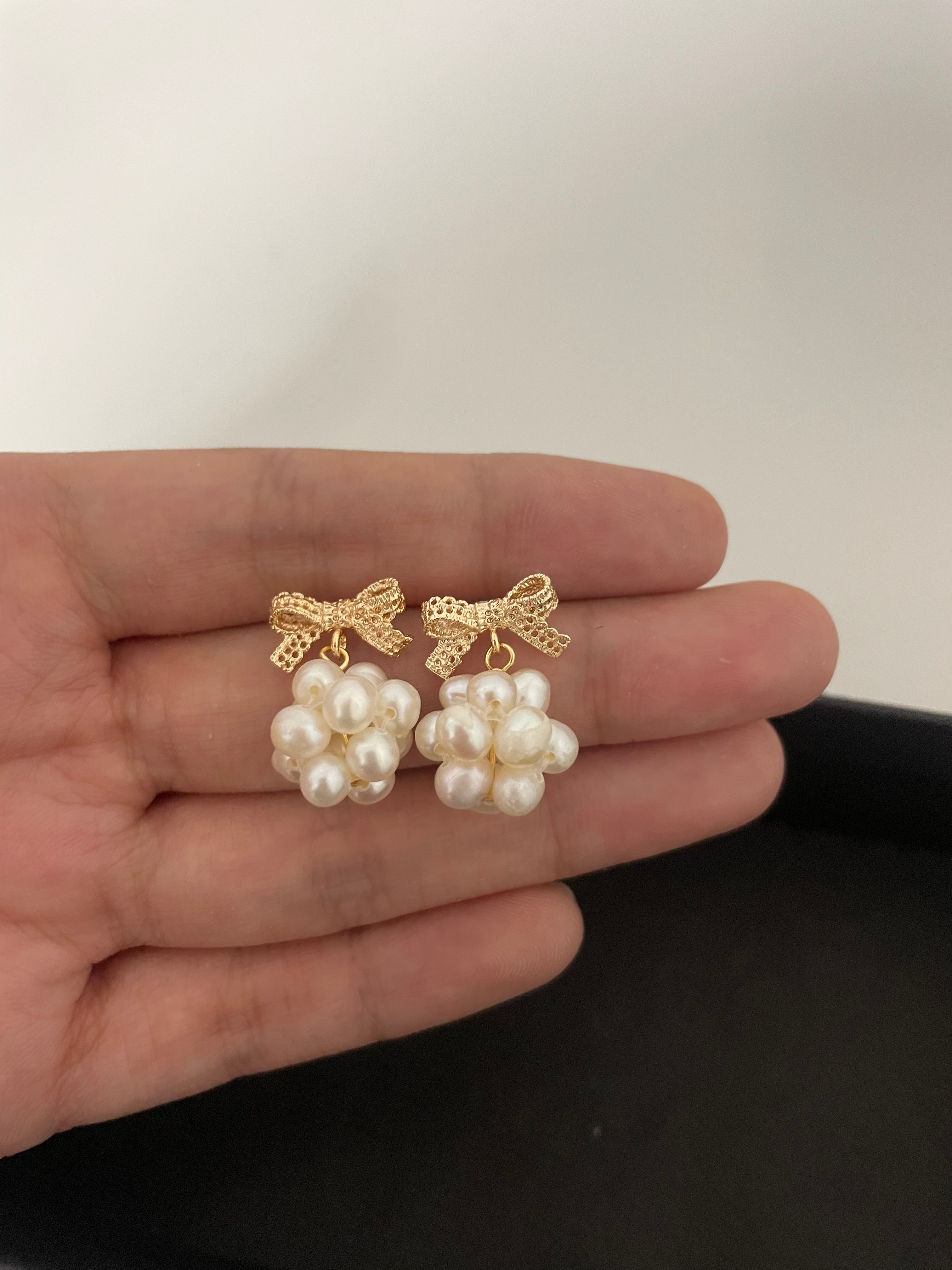 Gold-plated bowknot dangle earrings with clusters of freshwater pearls held in a hand.