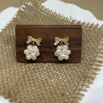Gold-plated bowknot dangle freshwater pearl earrings on a wooden block and burlap.