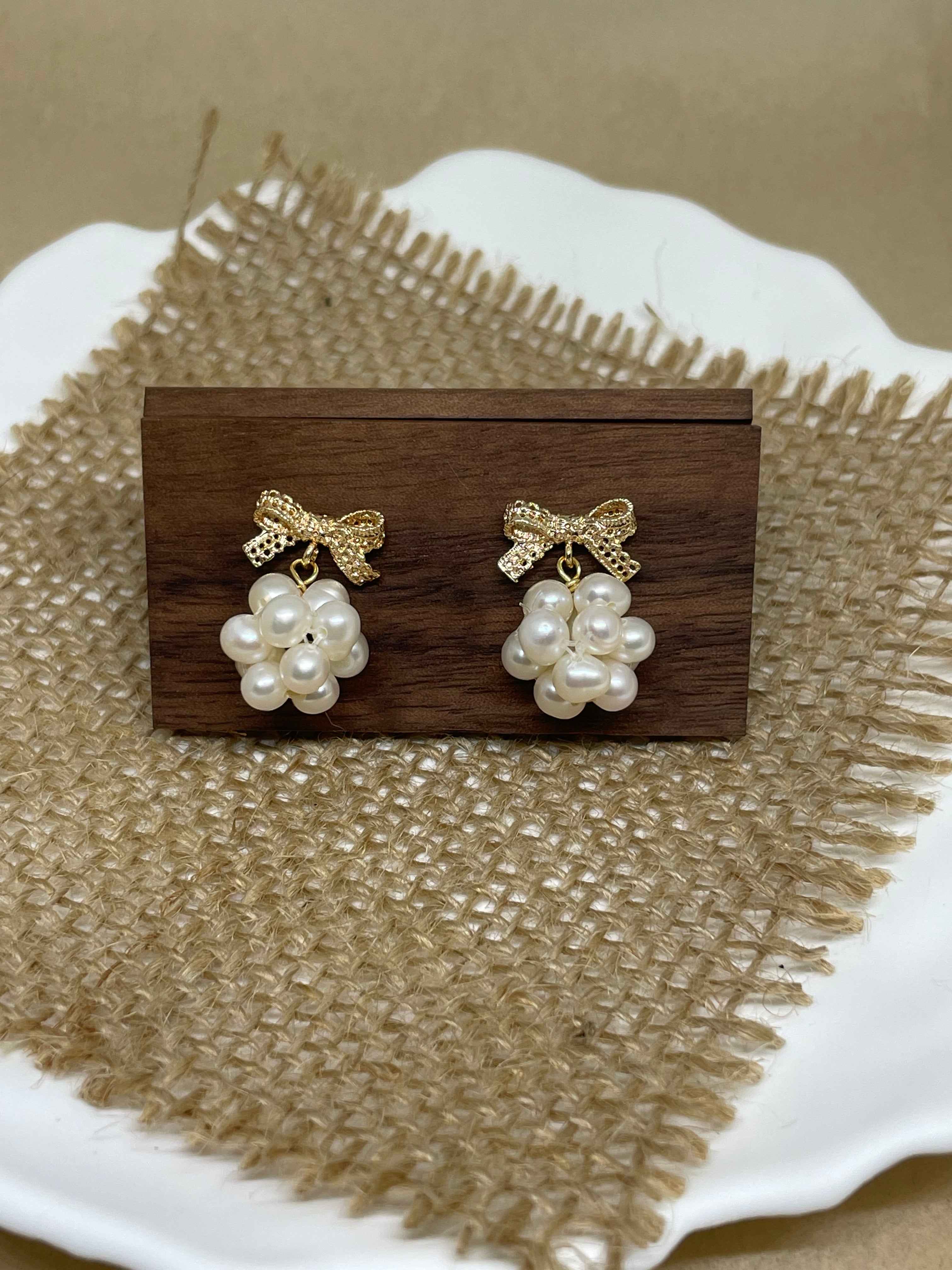 Gold-plated bowknot dangle freshwater pearl earrings on a wooden block and burlap.