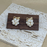 Two gold bowknot dangle freshwater pearl earrings are displayed on a wooden block.