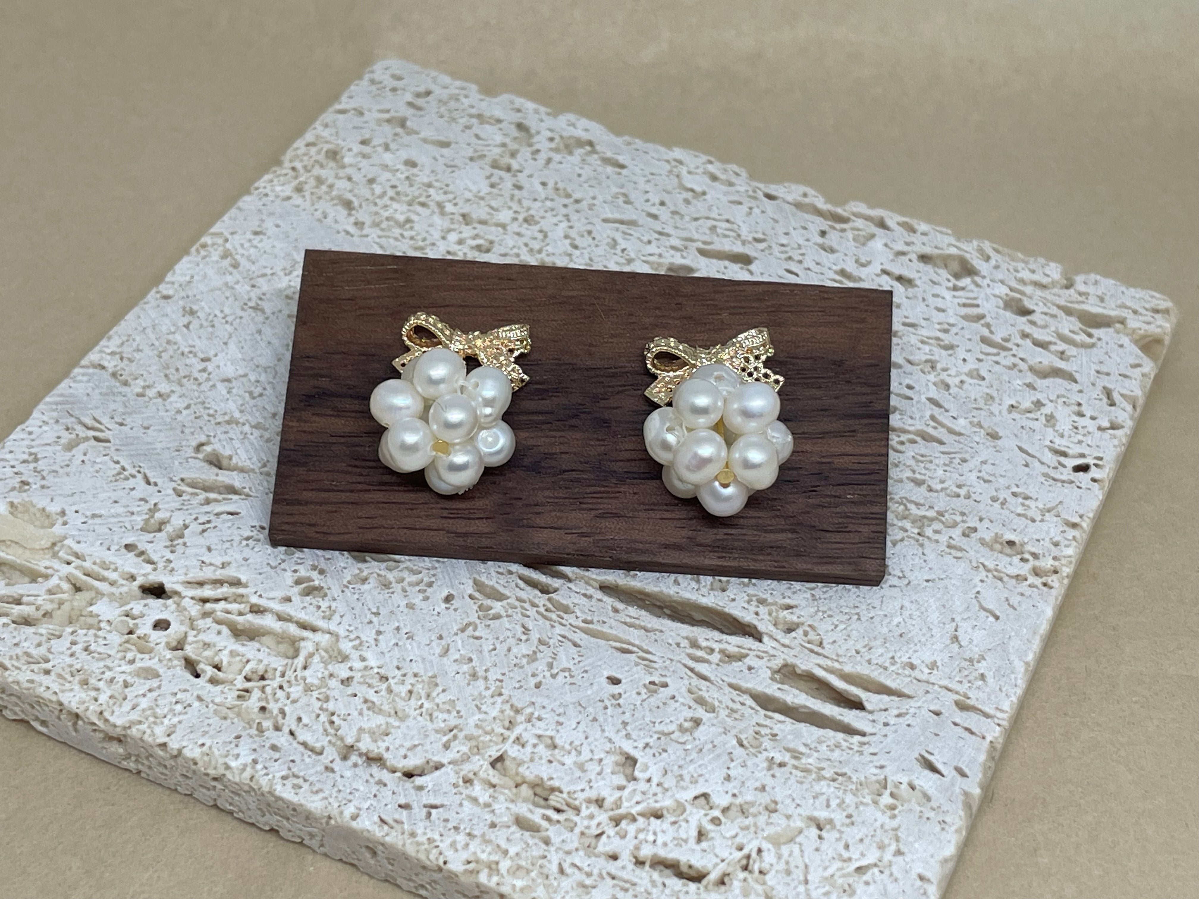 Two gold bowknot dangle freshwater pearl earrings are displayed on a wooden block.