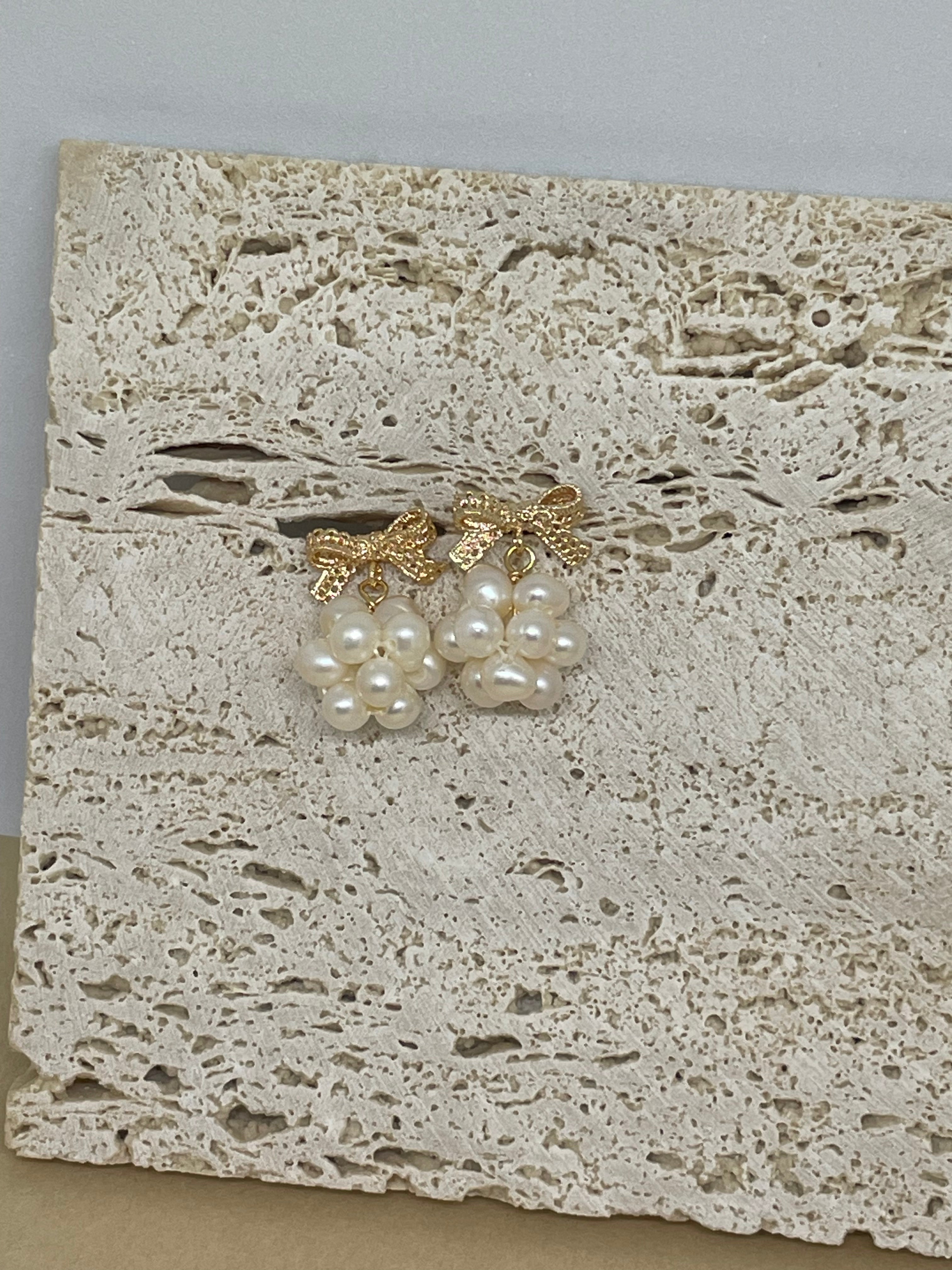 Gold-plated bowknot dangle freshwater pearl earrings on a textured stone surface.